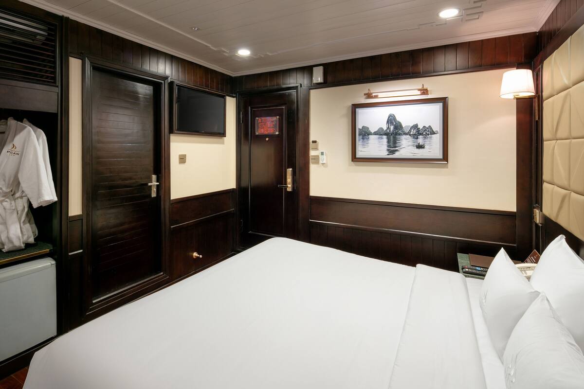 A hotel room with a large bed, a robe hanging on a door, a framed picture on the wall, and a bedside table with a lamp.