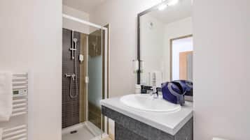 A modern bathroom with a glass-enclosed shower, a white sink, and a large mirror.