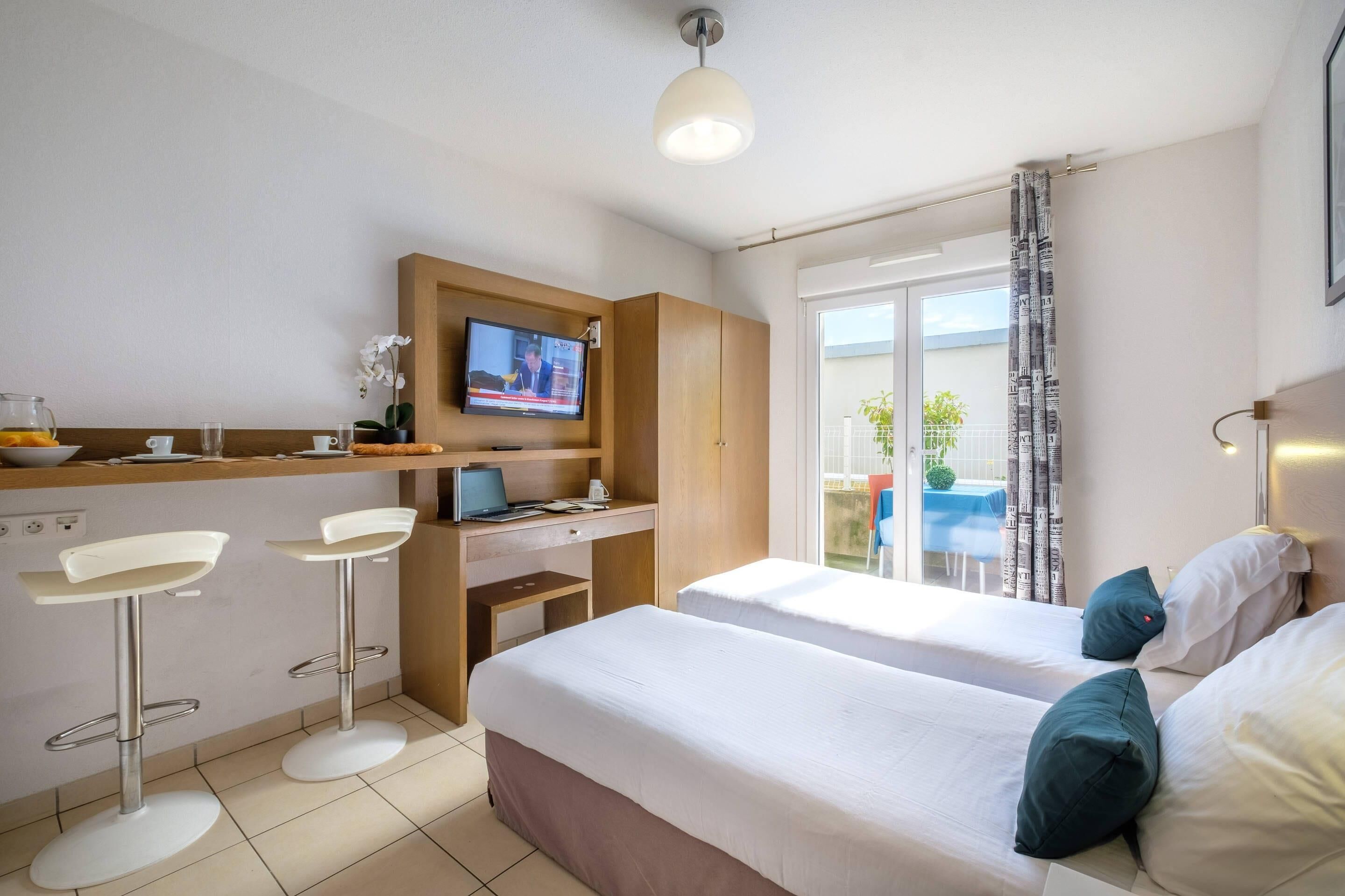 A hotel room with two beds, a desk with a computer, a TV, and a balcony with a view.
