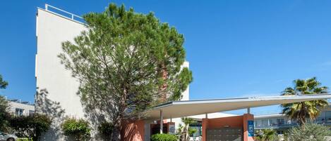 A modern building with a covered entrance, a parking area, and a clear blue sky.