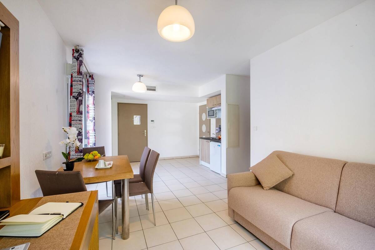 A modern living room with a beige sofa, a dining table with chairs, and a kitchen area in the background.