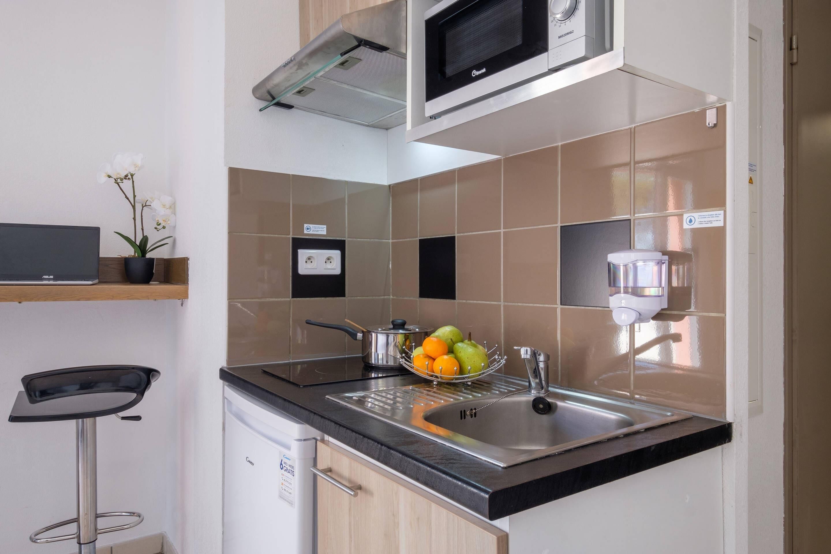 A kitchen with a microwave, sink, and a bowl of fruit on the counter.