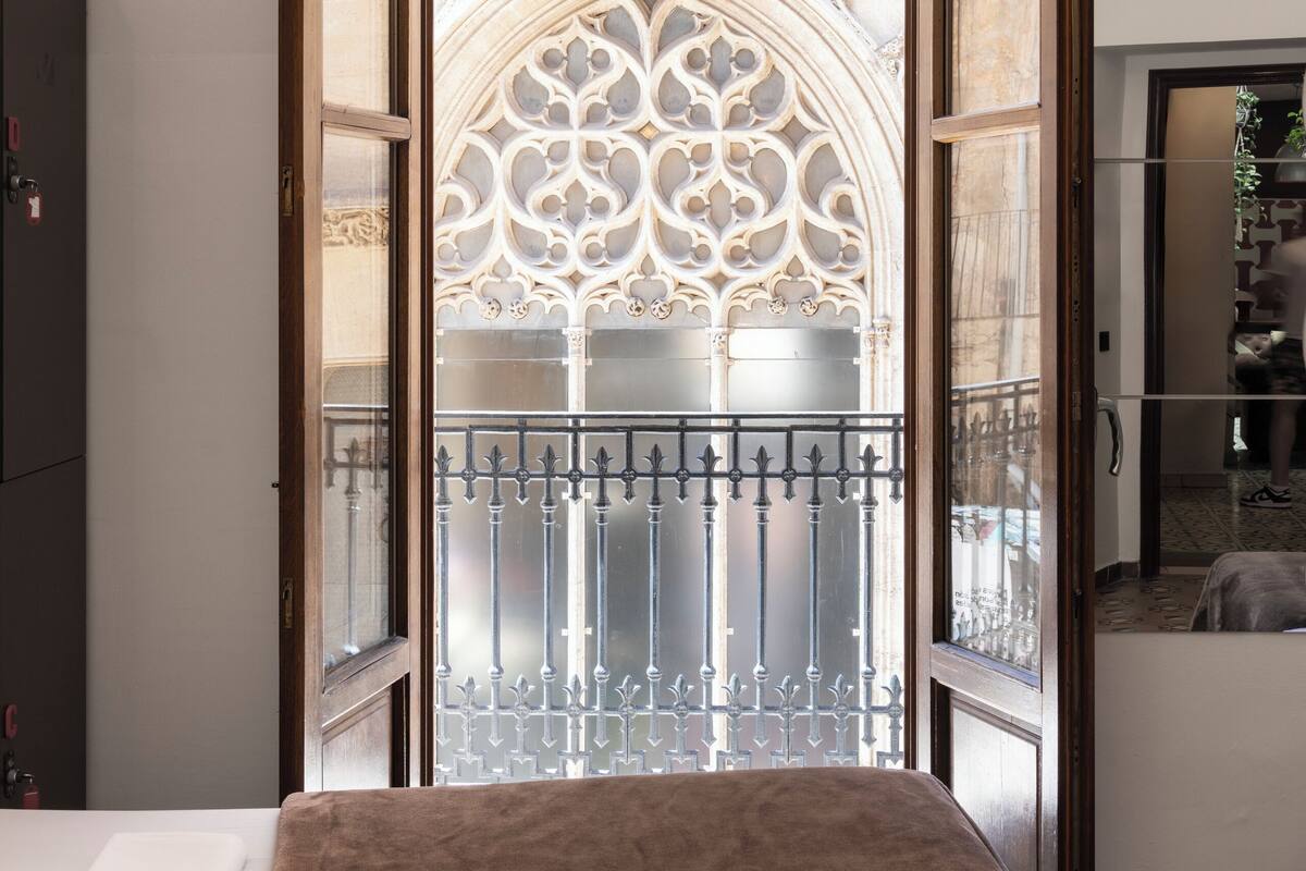 A room with a bed, a window with a decorative view, and a door leading to another area.
