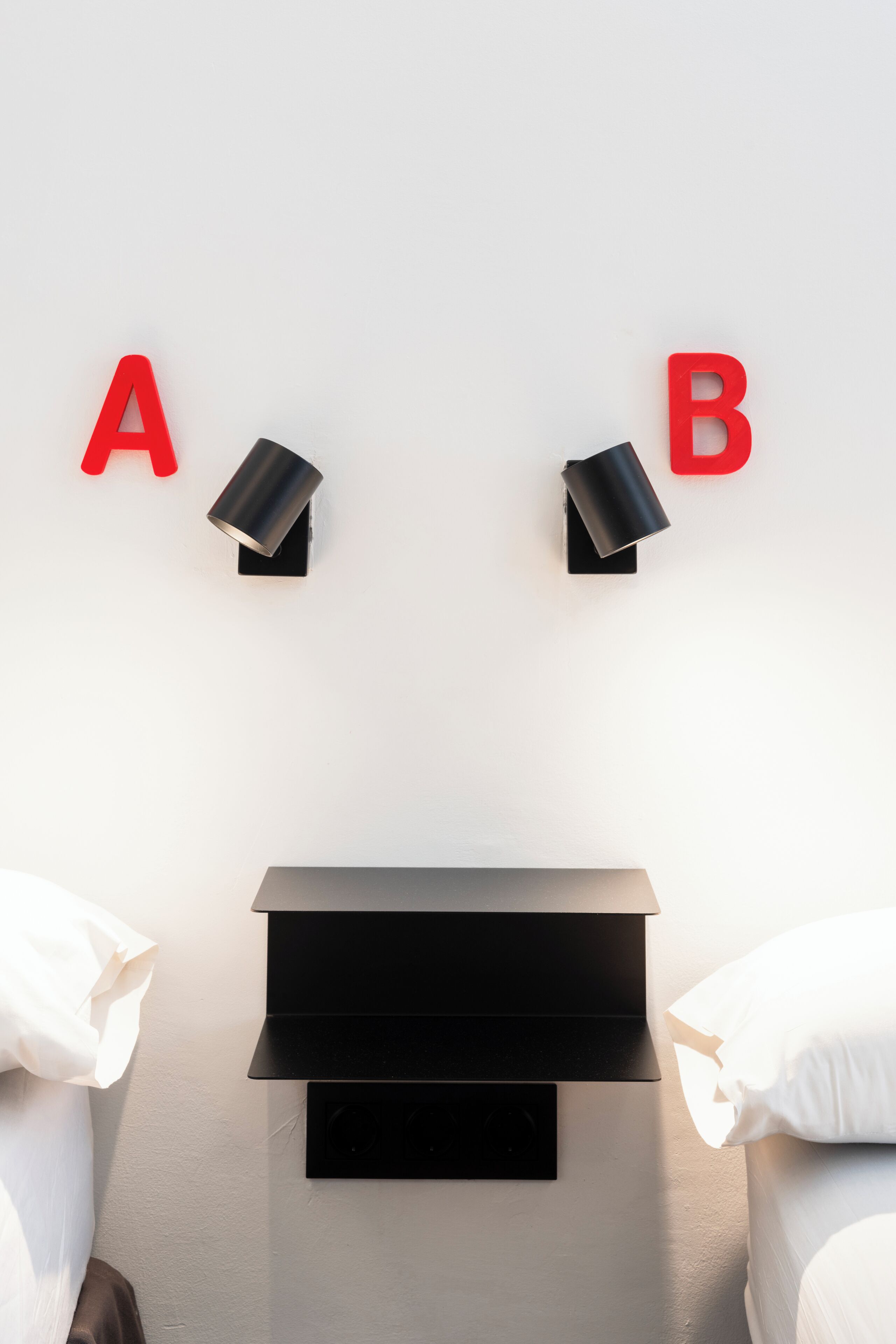 A room with a bed, a nightstand, and two wall-mounted lamps labeled 'A' and 'B'.
