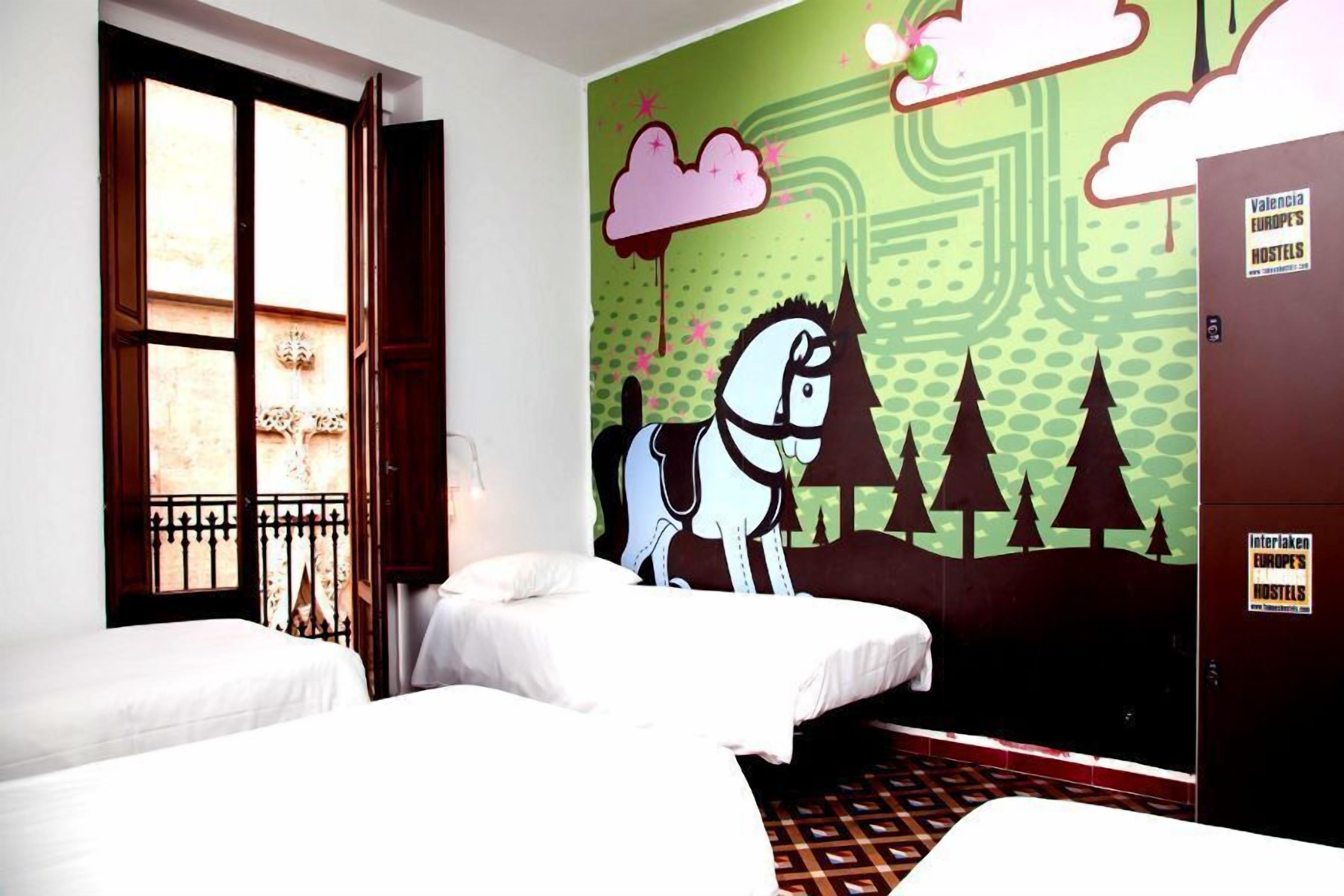 Una habitación con dos camas, una ventana con vistas y un mural de un caballo y árboles.
