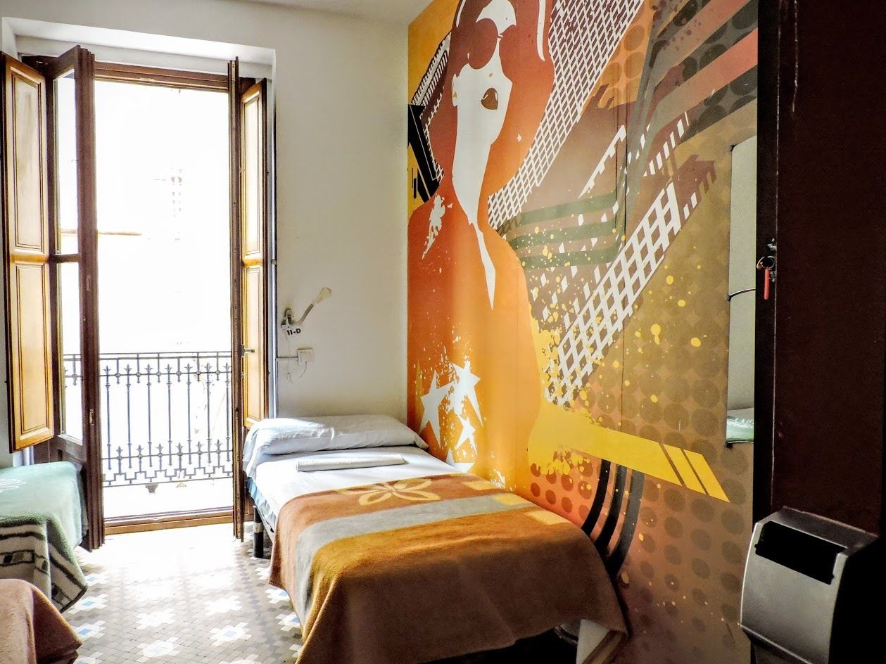 A room with two beds, a balcony, and a large mural on the wall.