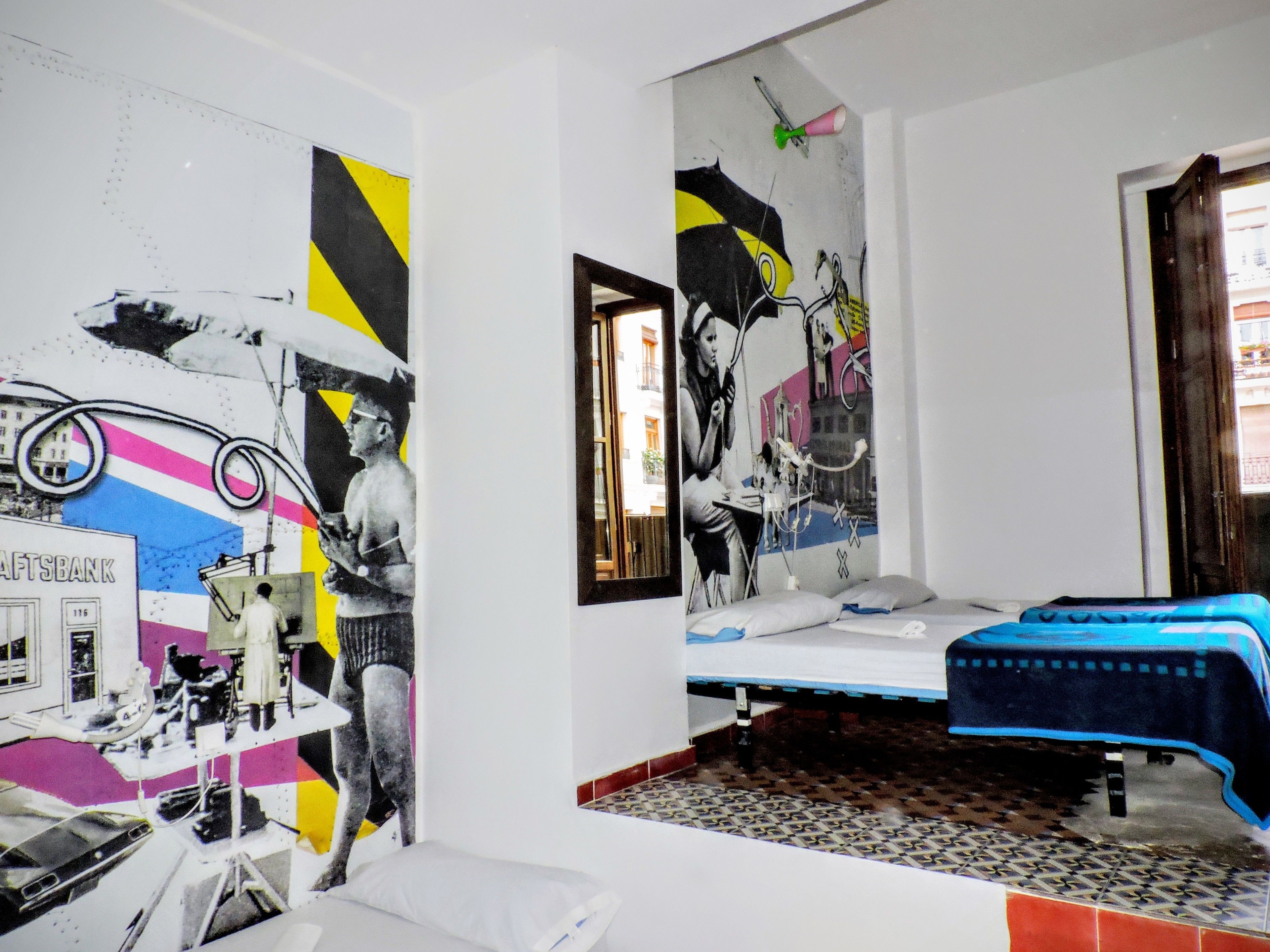 A room with a bed, a chair, and a wall with a large mural.