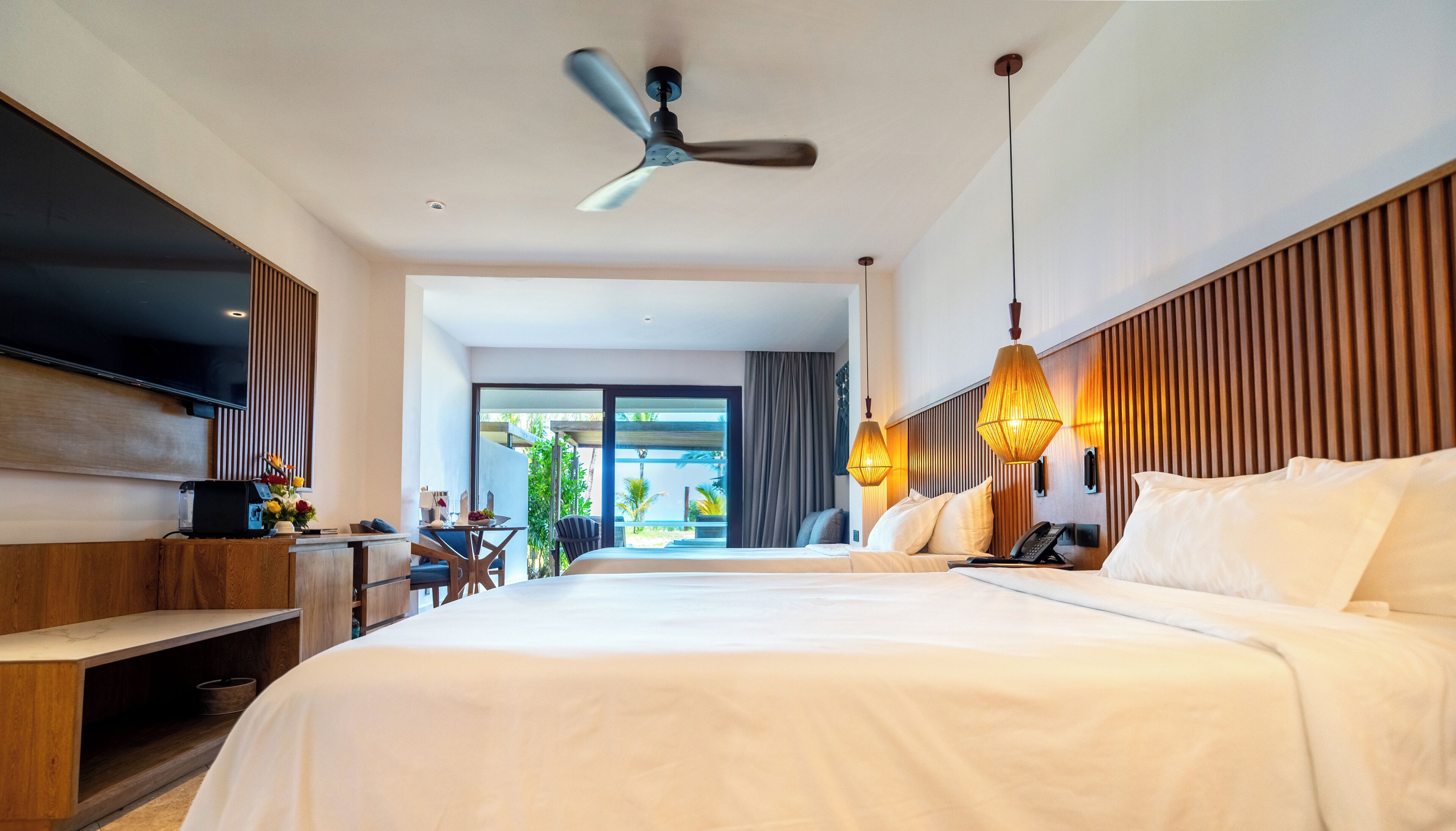 A hotel room with a bed, bedside table, TV, and a ceiling fan.