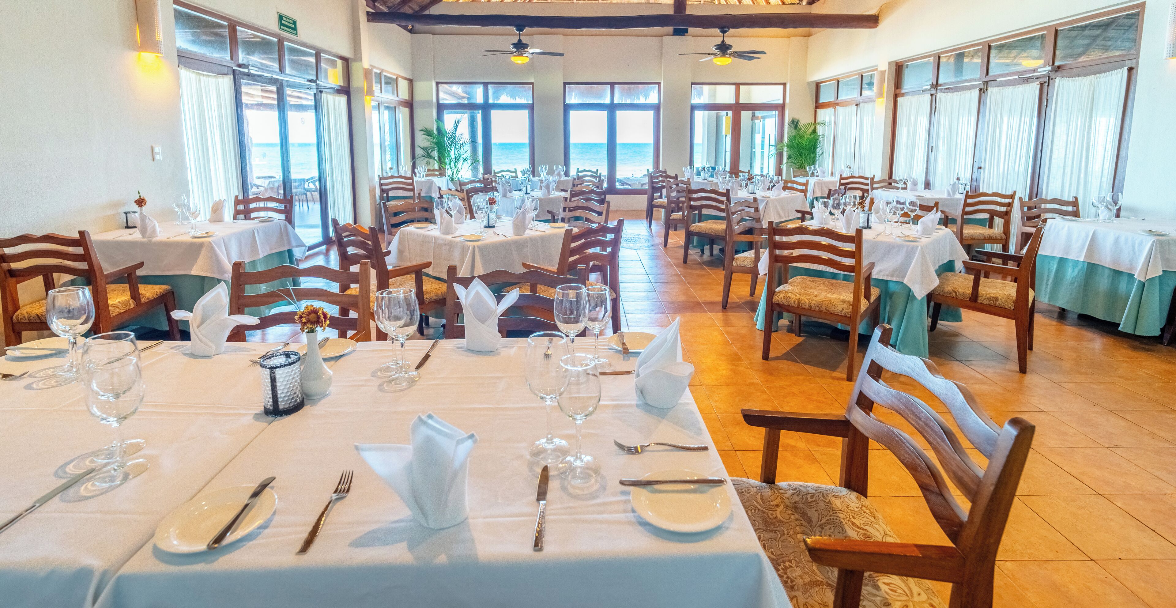 A restaurant with multiple tables, chairs, and a view of the ocean.