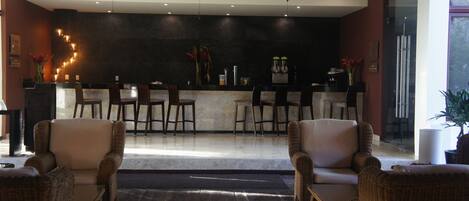 A modern lobby with wicker furniture, a bar area, ceiling fans, and a large window.