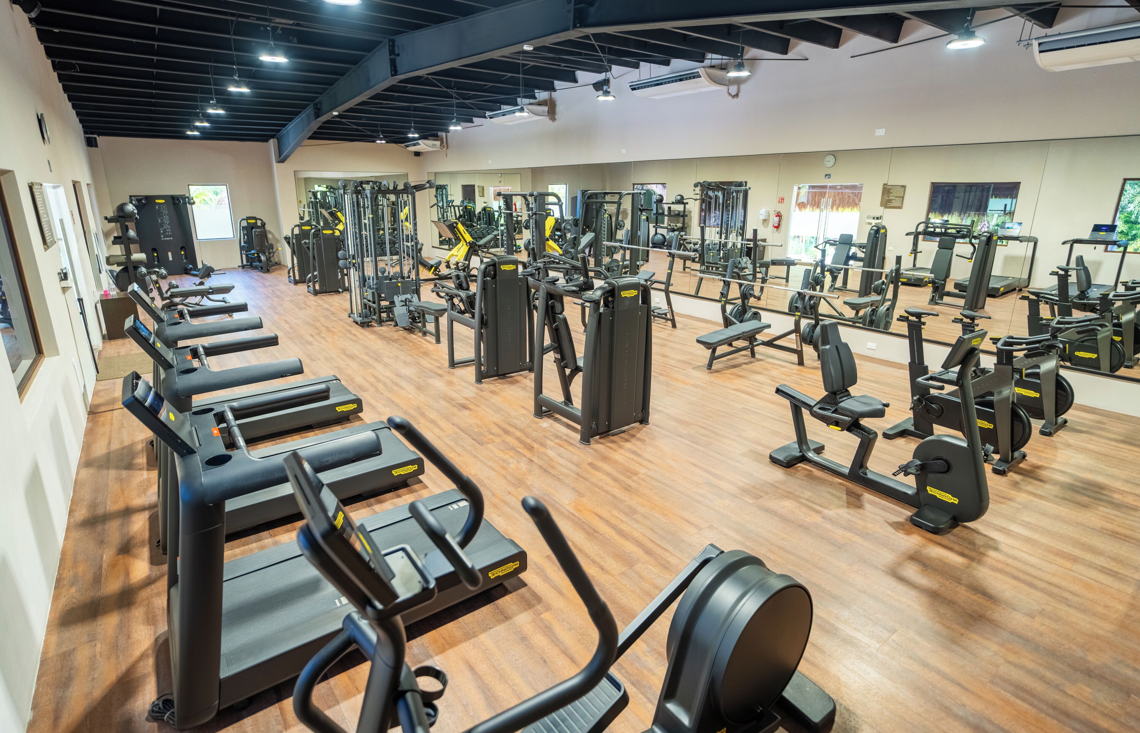 A gym with various exercise equipment, including treadmills and weight machines, arranged on a wooden floor.