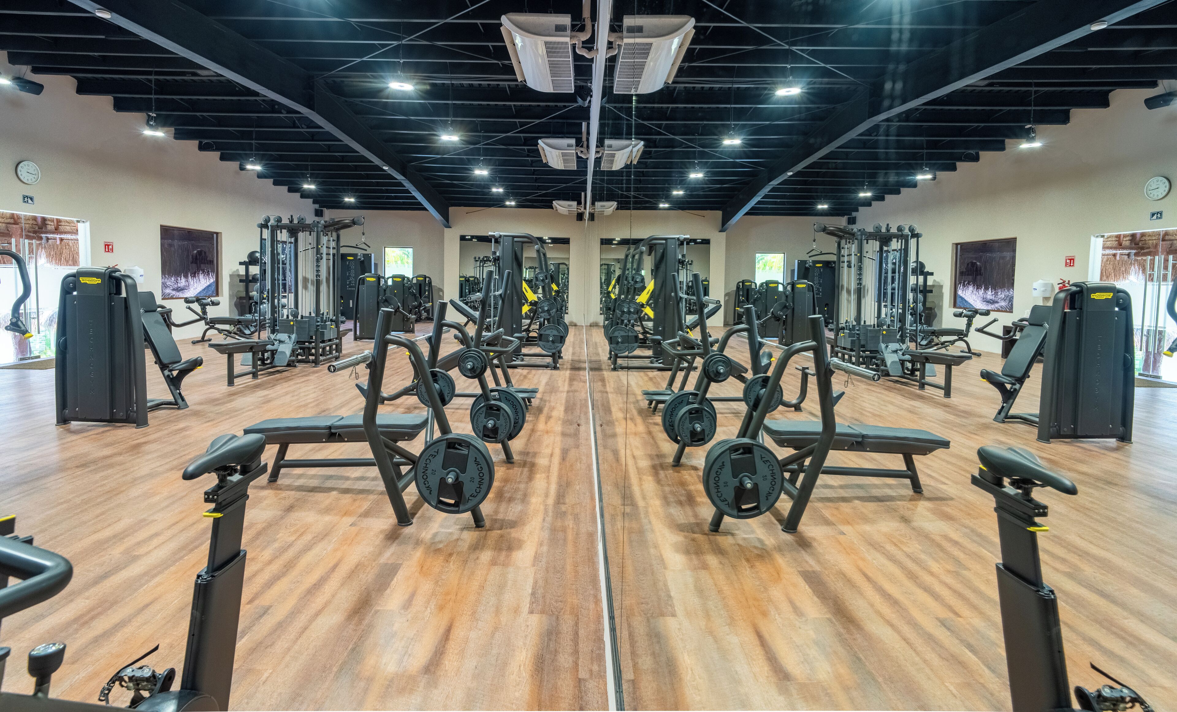 A gym with mirrored walls, weightlifting equipment, and a wooden floor.