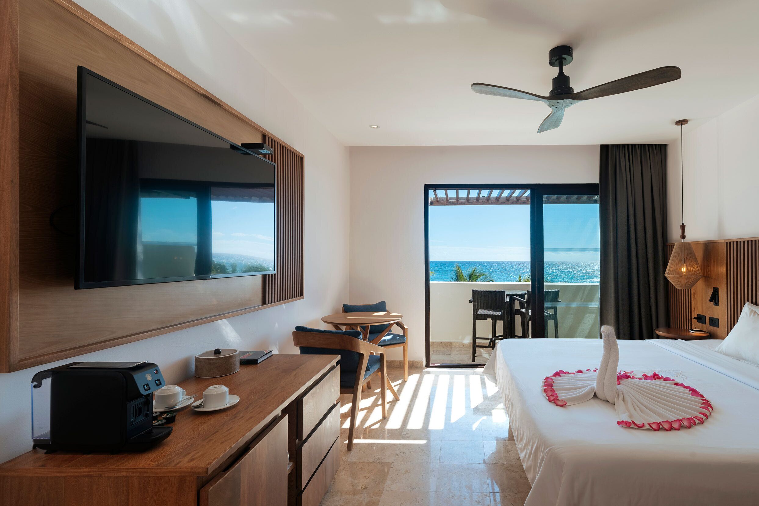 A hotel room with a bed, a desk with a coffee maker, a TV, and a view of the ocean.