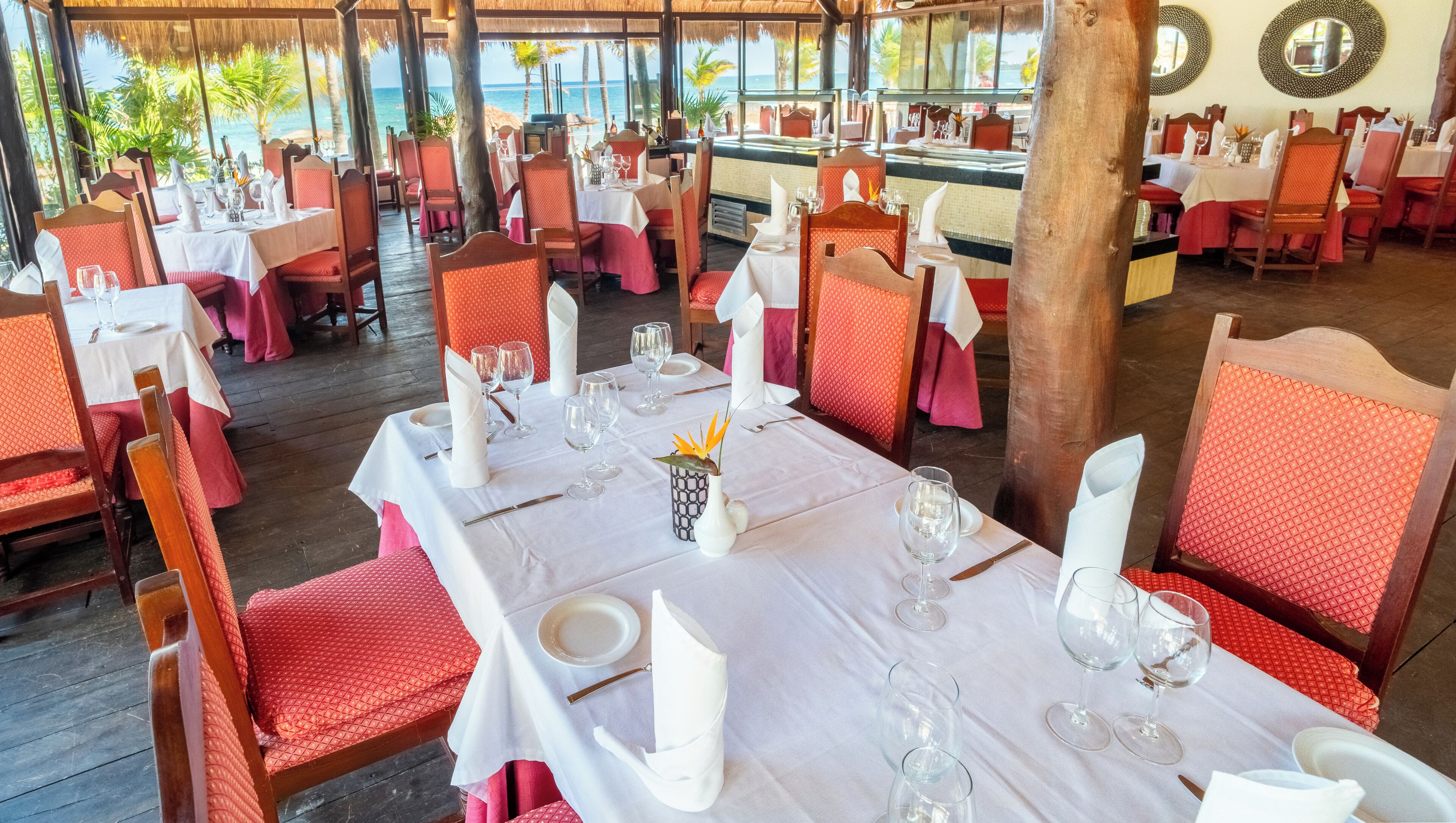 A restaurant with tables set for dining, chairs, and a view of the ocean.