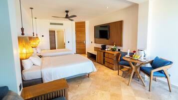A hotel room with two beds, a desk, a chair, a TV, and a ceiling fan.
