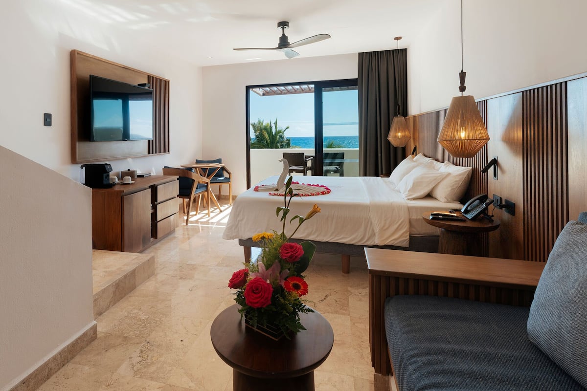 Una habitación de hotel moderna con cama, escritorio, televisor y balcón con vista al mar.