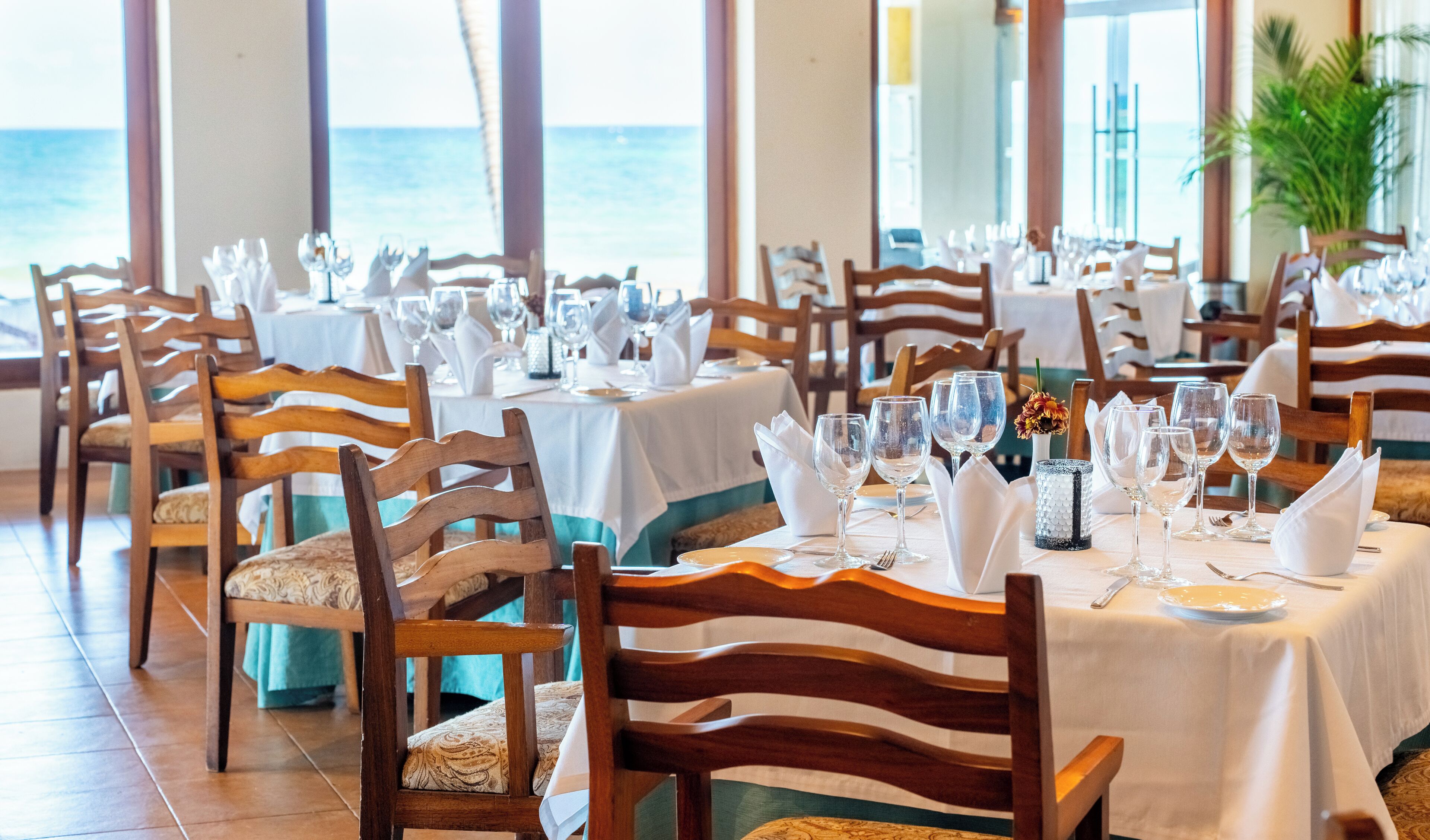 Un restaurant avec des tables dressées, des chaises et une vue sur l’océan.