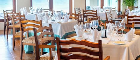 Un restaurante con mesas dispuestas para comer, sillas y vista al océano.