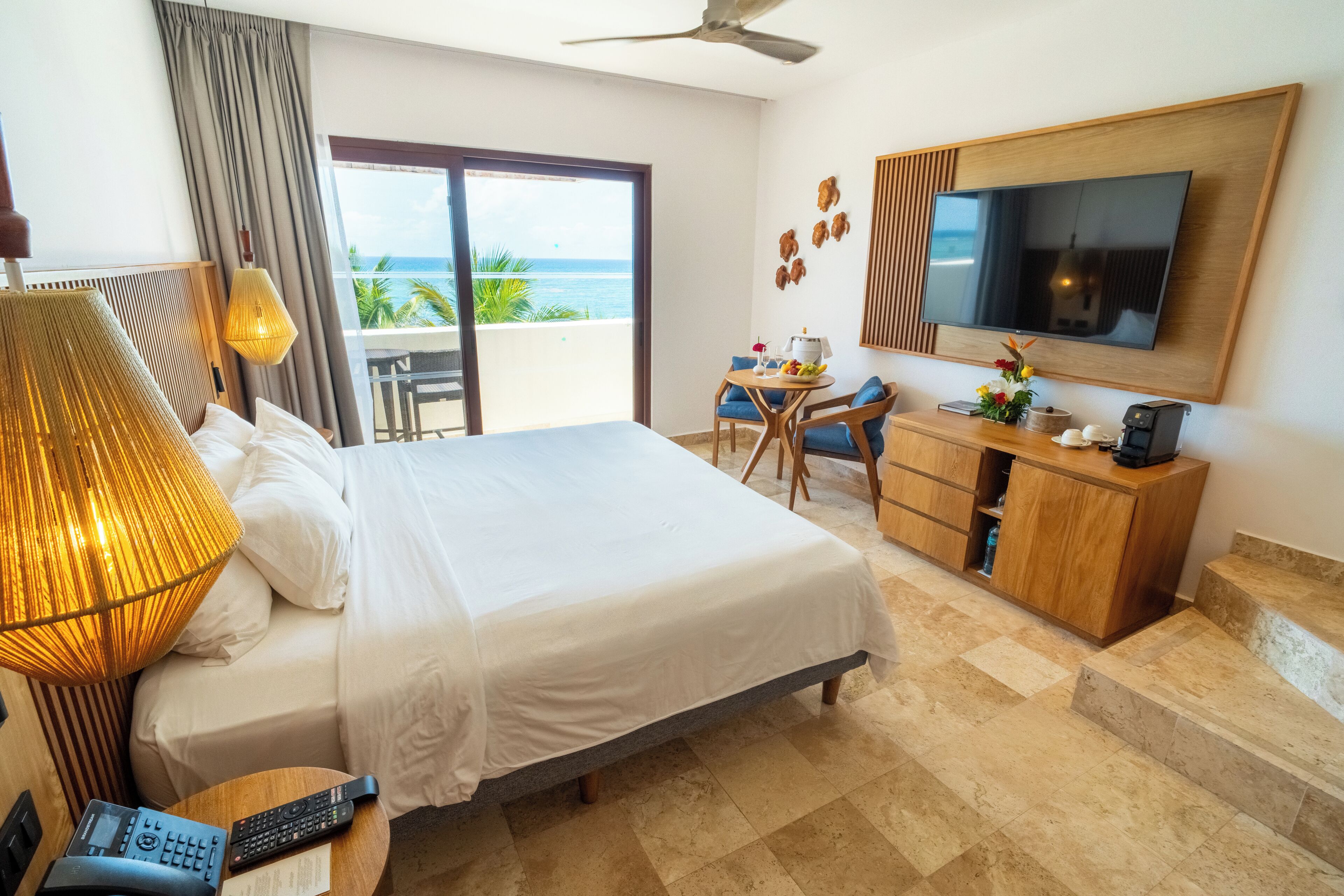 Habitación de hotel con cama, escritorio, televisor y balcón con vista al océano.