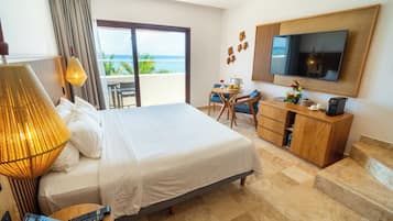 Habitación de hotel con cama, escritorio, televisor y balcón con vista al océano.