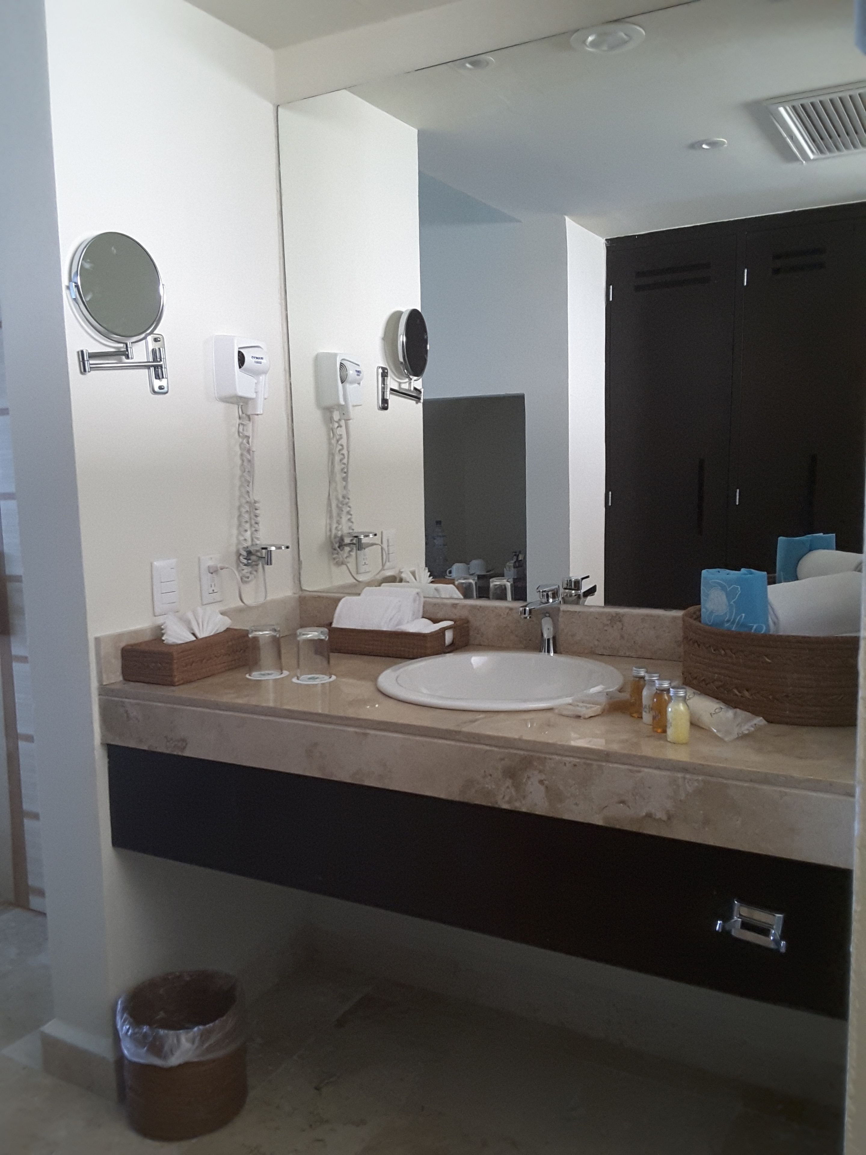 A modern bathroom with a large mirror, a sink, a hairdryer, and a towel rack.