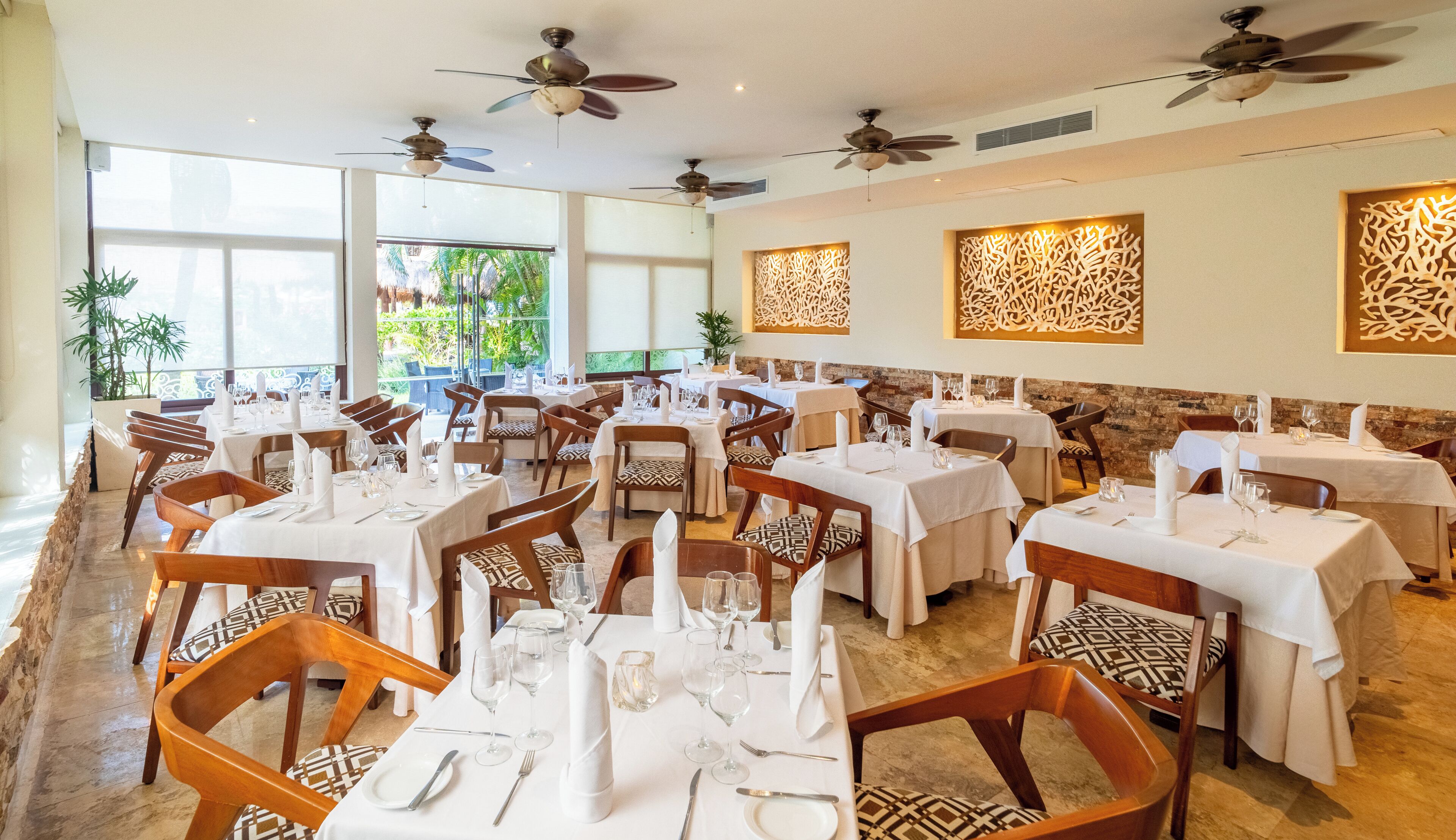 Restaurante com várias mesas, ventiladores de teto e painéis decorativos na parede.
