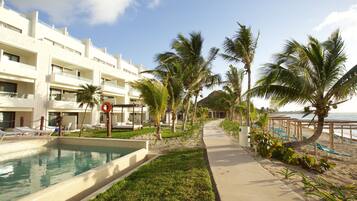 A pool area with a clear view of the sea, a pathway lined with palm trees, and a building with multiple balconies.