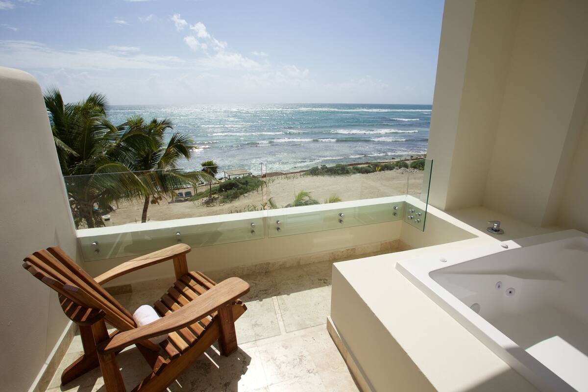 Un balcón con vista al océano, una silla de madera y una bañera.