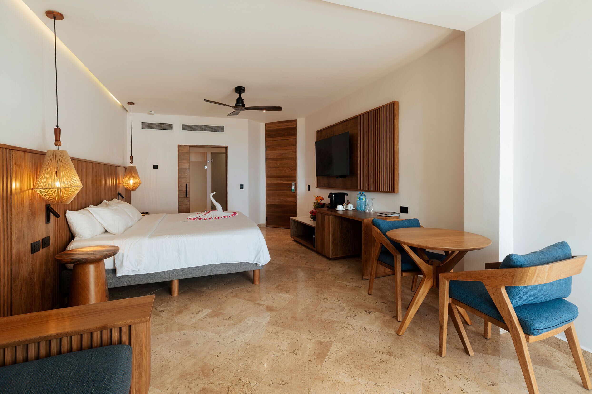 Una habitación de hotel con cama, escritorio, silla, televisor y ventilador de techo.