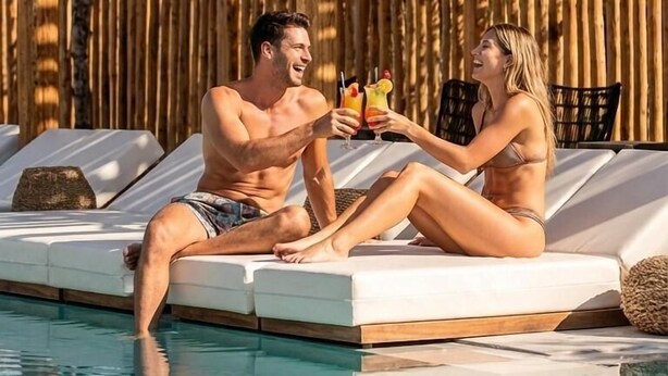 Una pareja descansando junto a una piscina con pérgolas de madera y luces colgantes.