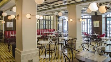 Um restaurante com chão xadrez, mesas redondas e cabines vermelhas.