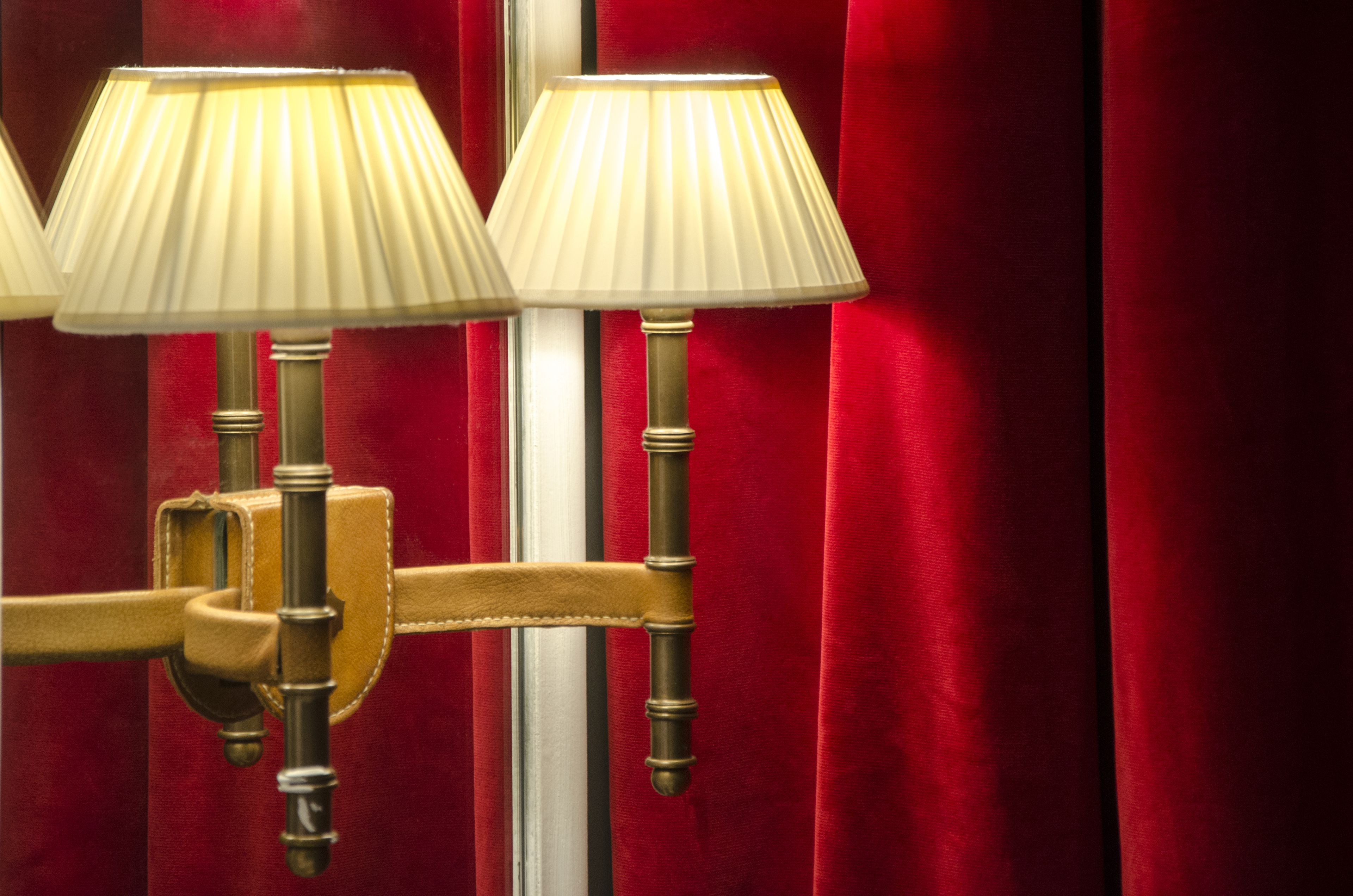 A wall-mounted lamp with a classic design, featuring three lampshades and a brass finish.