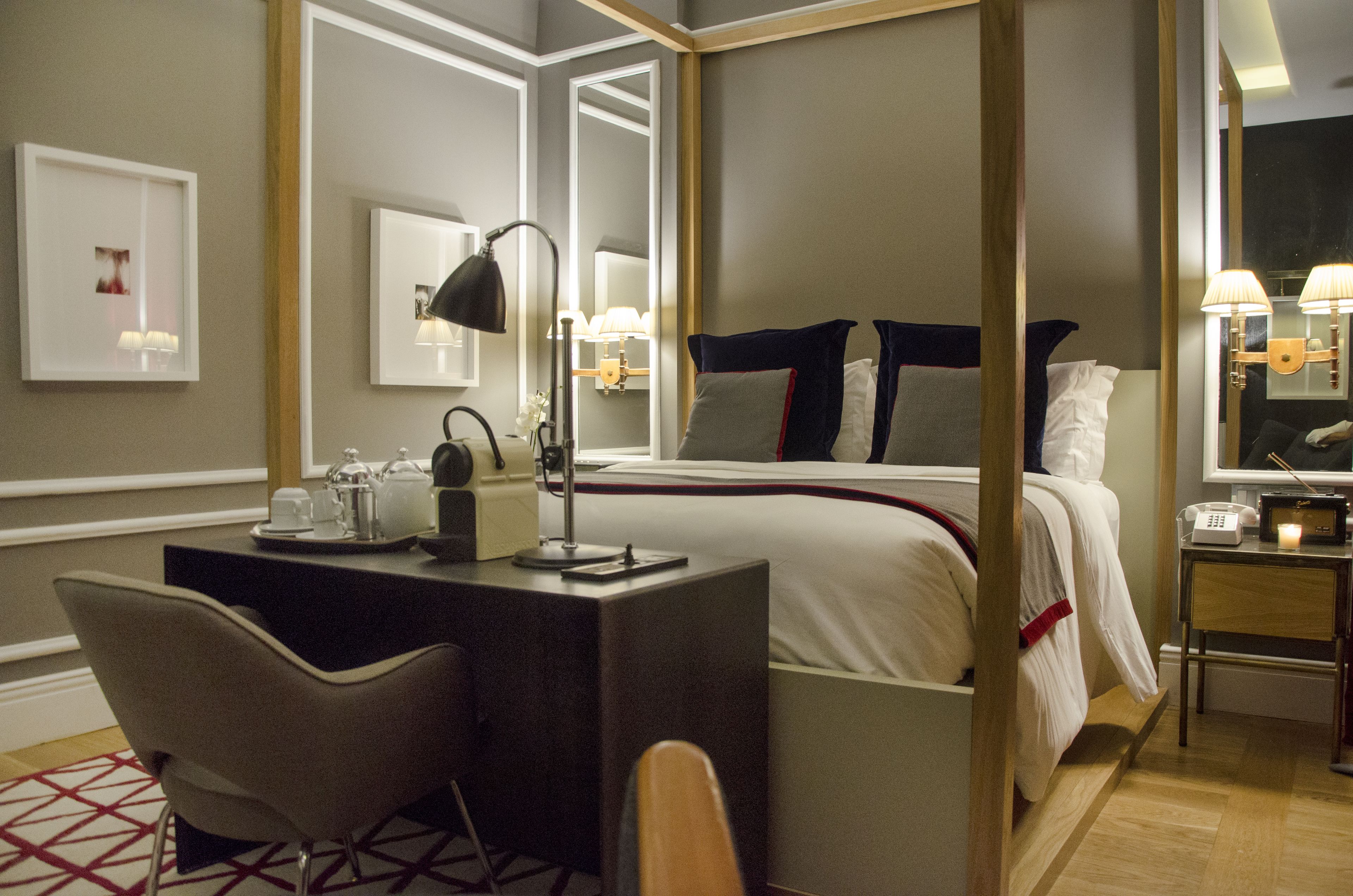 Et hotelværelse med himmelseng, et skrivebord med lampe, en stol og et natbord med telefon og et stearinlys.