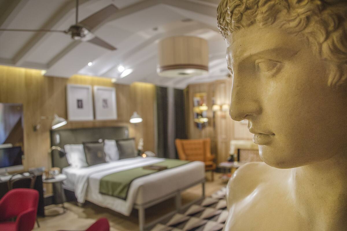 Una habitación de hotel con una cama, un escritorio, una silla y una estatua.