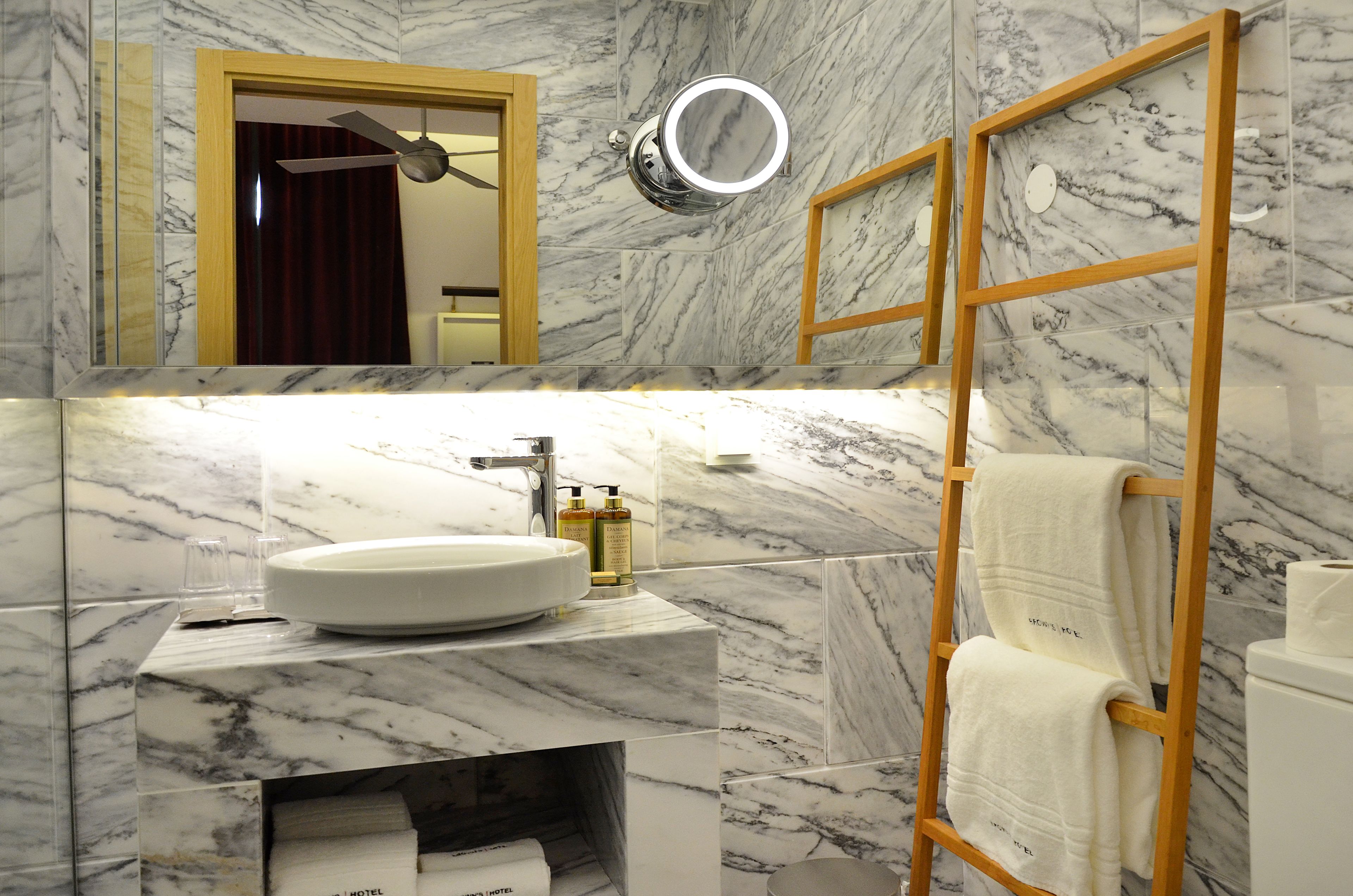 A bathroom with a marble sink, a wooden towel rack, and a mirror with a light.
