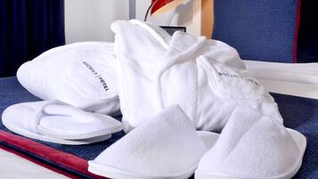 A bed with white slippers and a white robe, a red lamp, and a blue chair.