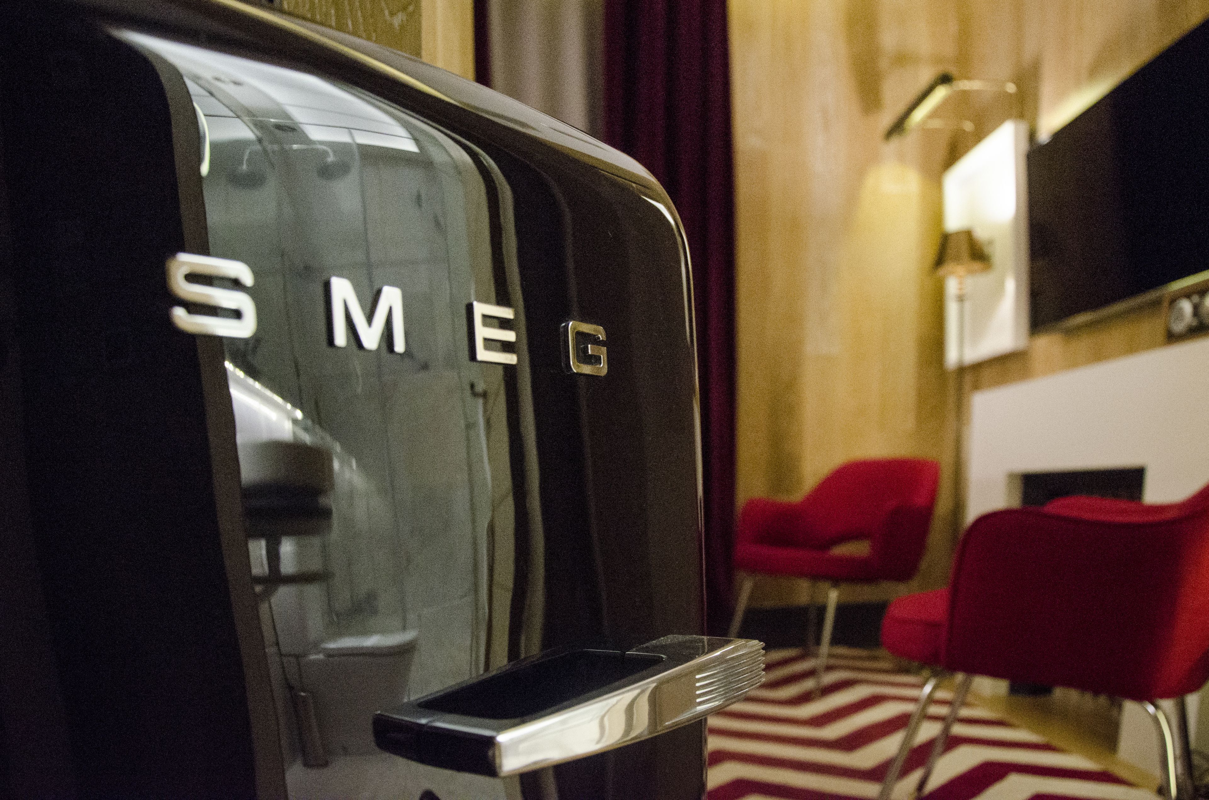 Una stanza con un frigorifero Smeg nero, sedie rosse e un tappeto a righe.