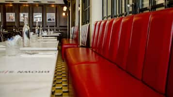Interior de restaurante con asientos tapizados en rojo, piso a cuadros y mesas dispuestas con botellas y vasos.