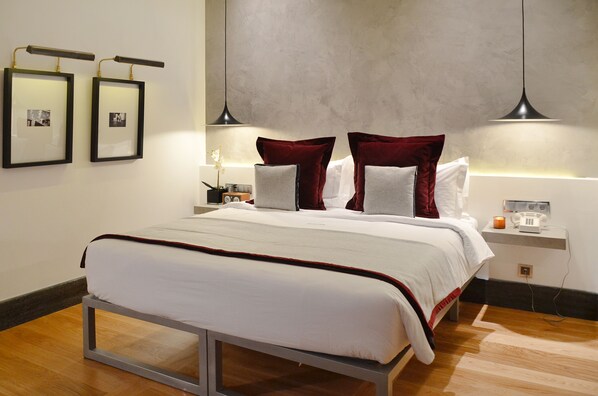 Una cama bien hecha con una colcha blanca y roja, dos cuadros en la pared y una mesita de noche con una lámpara y un teléfono.