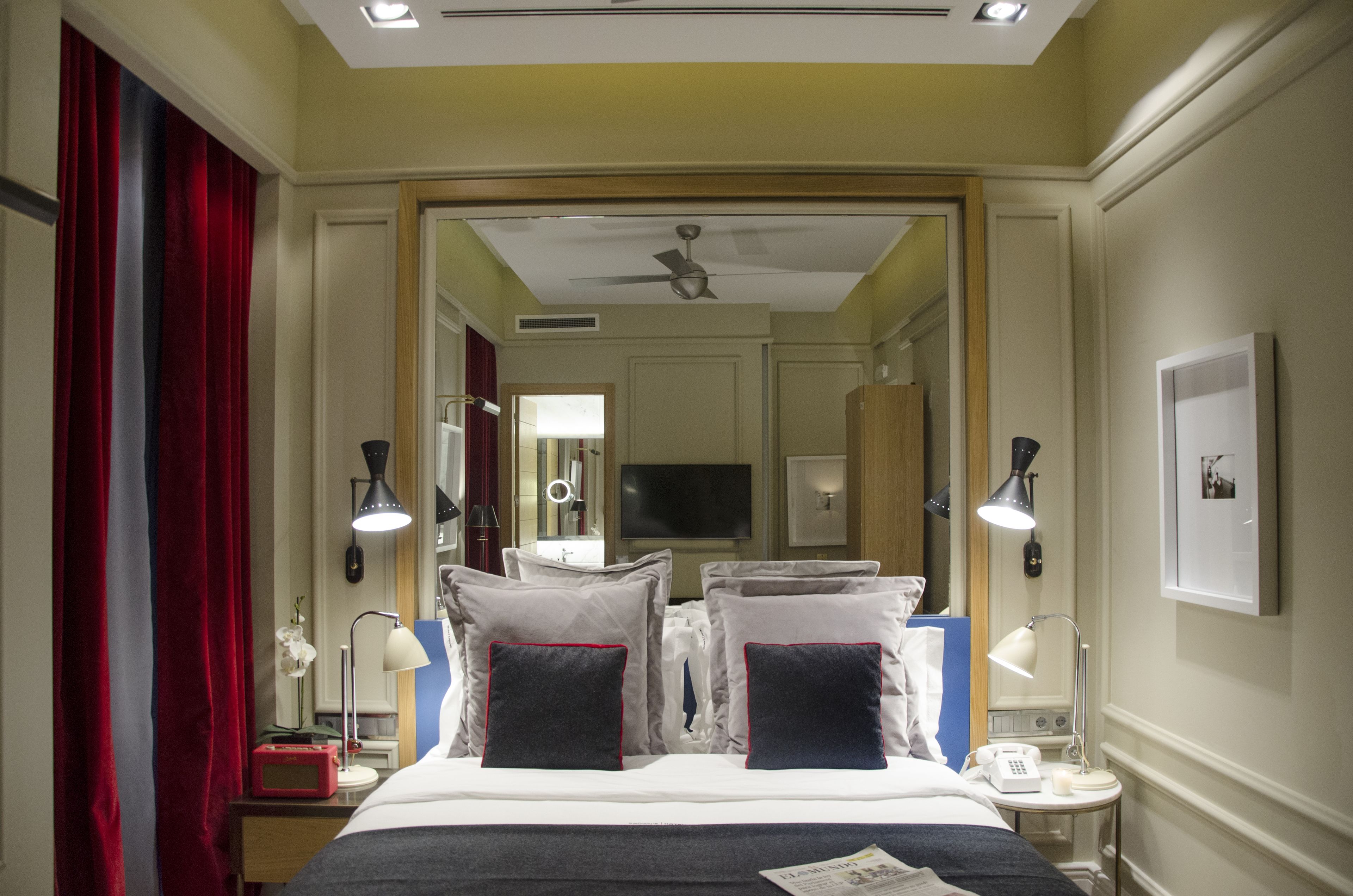 A hotel room with a bed, bedside lamps, a telephone, a mirror, and a television.