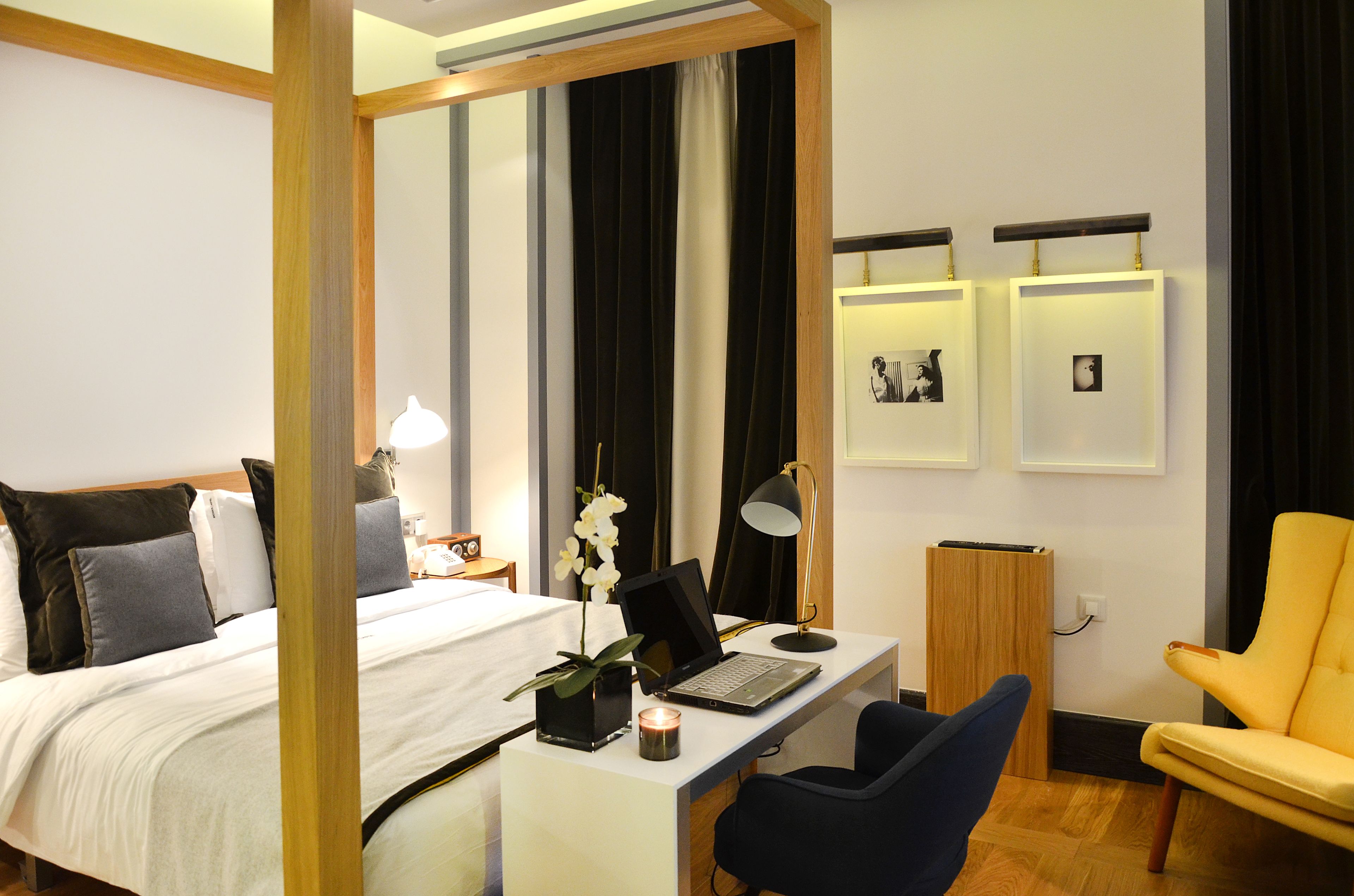 Habitación de hotel con cama, escritorio, computadora portátil, silla y una pequeña mesa con una vela.