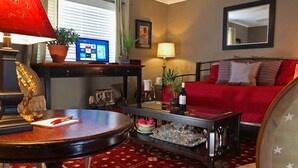 Una sala de estar con un sofá rojo, una mesa de centro de madera, un televisor sobre un mueble, una lámpara y una planta en maceta.