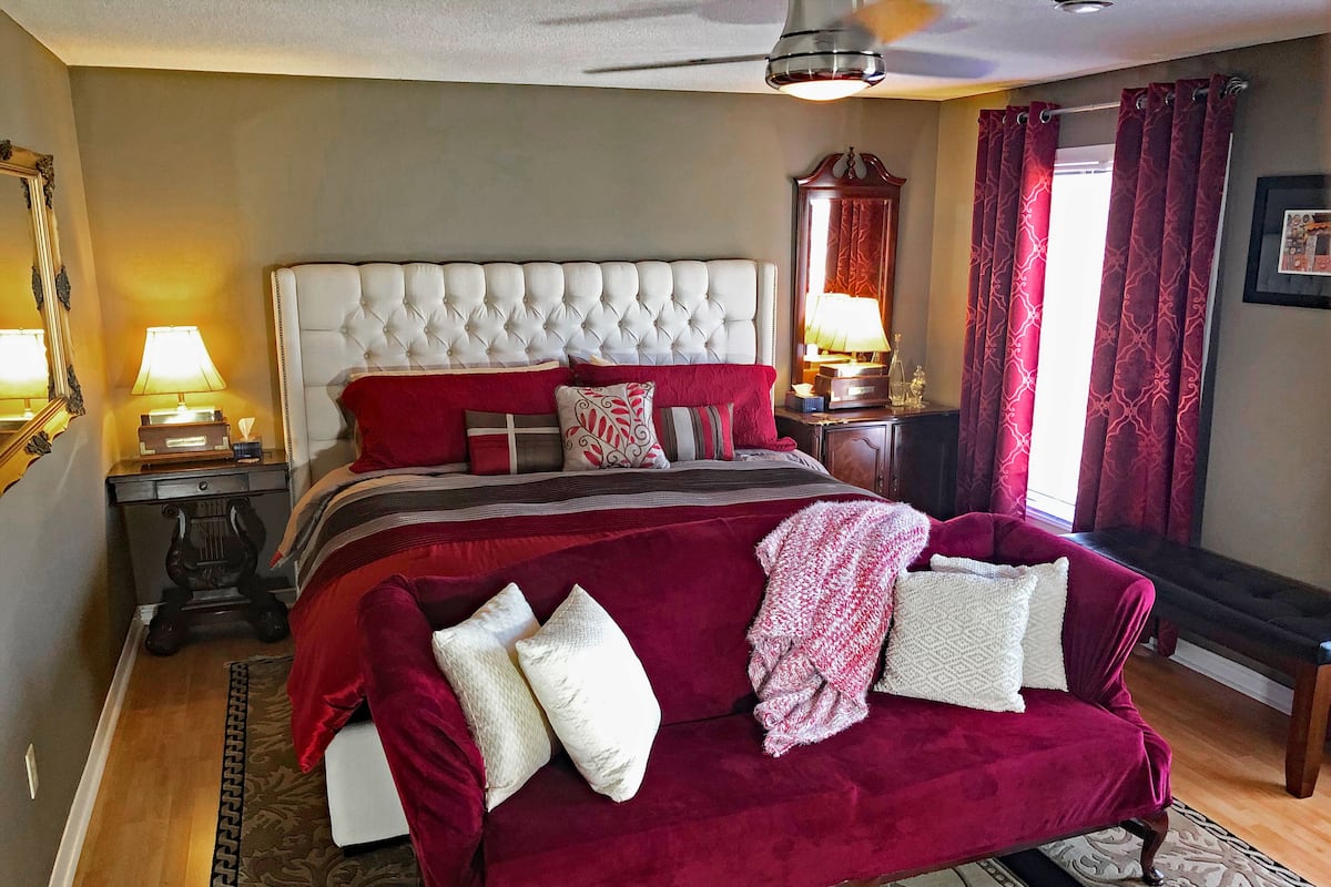 A bedroom with a tufted headboard, a red velvet sofa, and a large bed with multiple pillows.