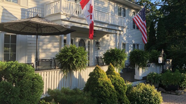Una casa de dos plantas con un porche, una bandera y un jardín bien cuidado.