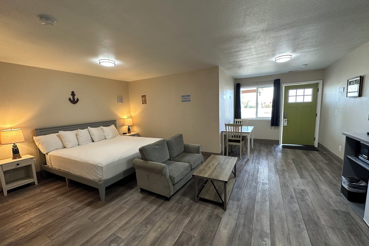 Un dormitorio con cama, mesitas de noche, un sofá, una pequeña mesa y un comedor con sillas.