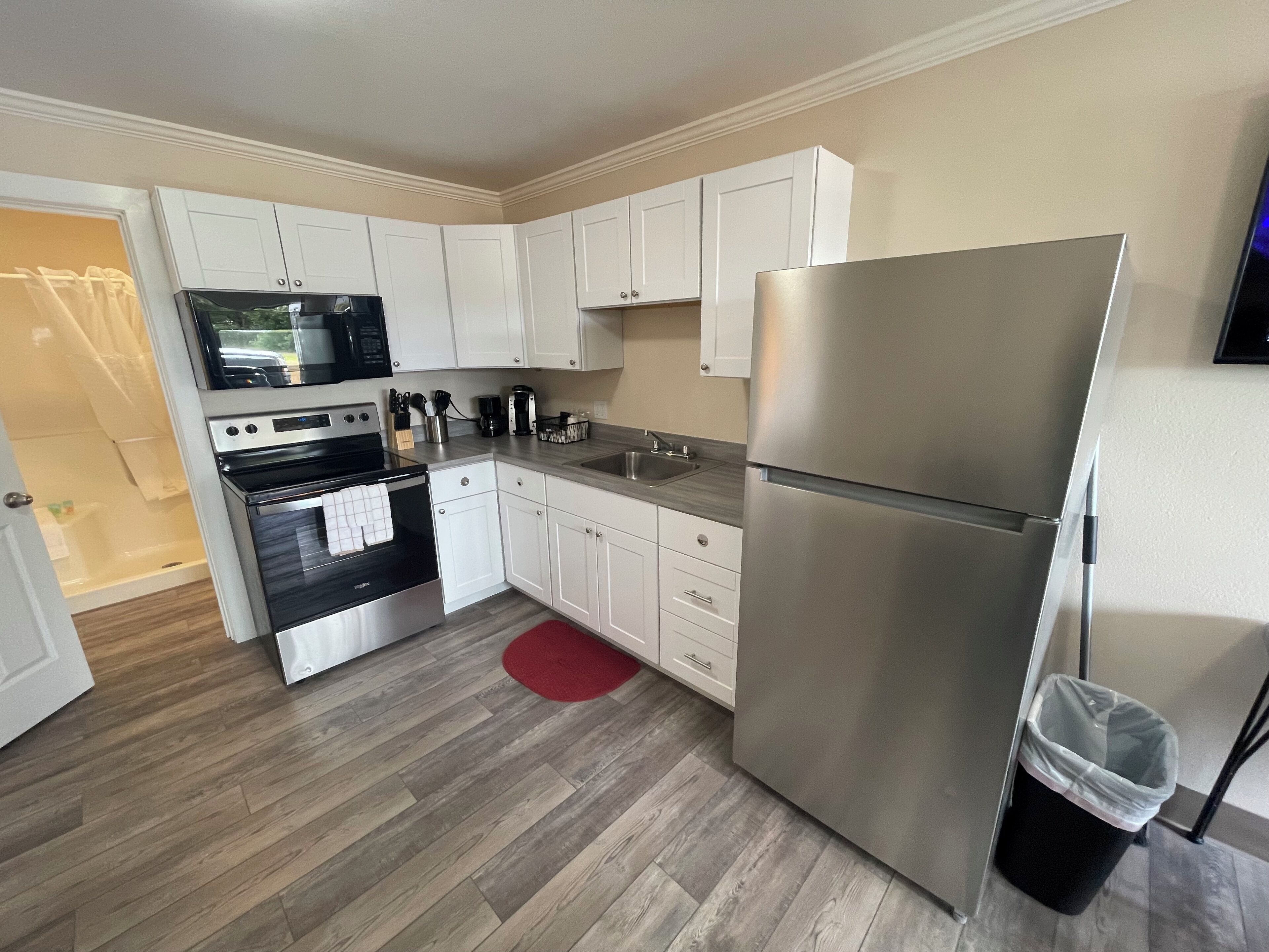 Una cocina compacta con armarios blancos, un refrigerador de acero inoxidable, un microondas, un horno y un lavamanos.