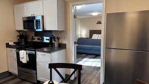 A compact kitchen with a microwave, stove, and refrigerator, leading to a living area with a sofa and a lamp. - The Coastal Inn and Suites (Long Beach)