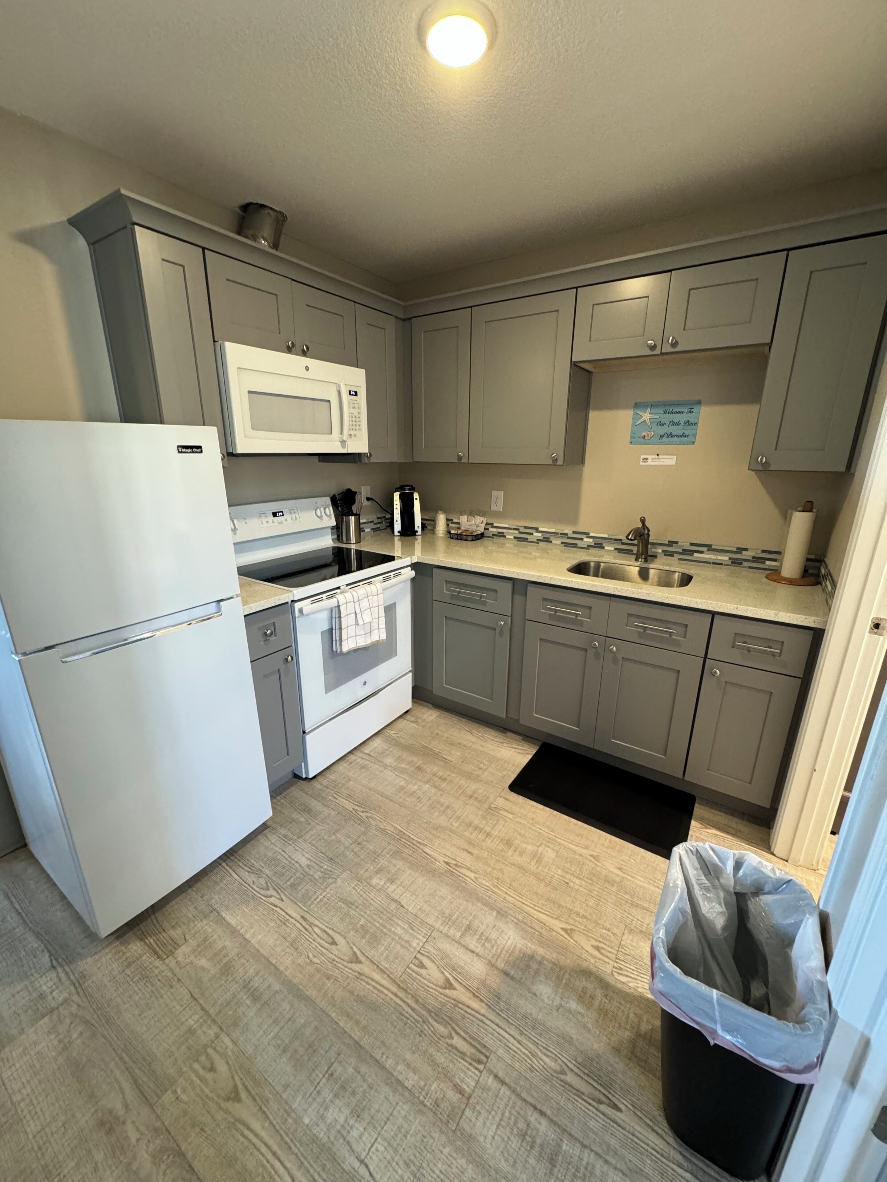 A compact kitchen with grey cabinets, a white refrigerator, a microwave, a stove, and a sink.