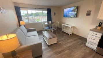 Una sala de estar moderna con sofá, mesa de centro y televisor. Se ve una ventana con cortinas, una mesita y un televisor en la pared.