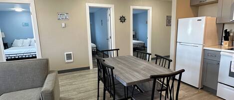 A compact living space with a dining table, chairs, a sofa, a kitchenette, and a bedroom visible through an open door.